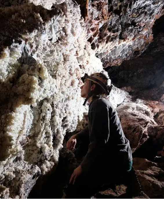 A caver examining white mineral formations on a cave wall